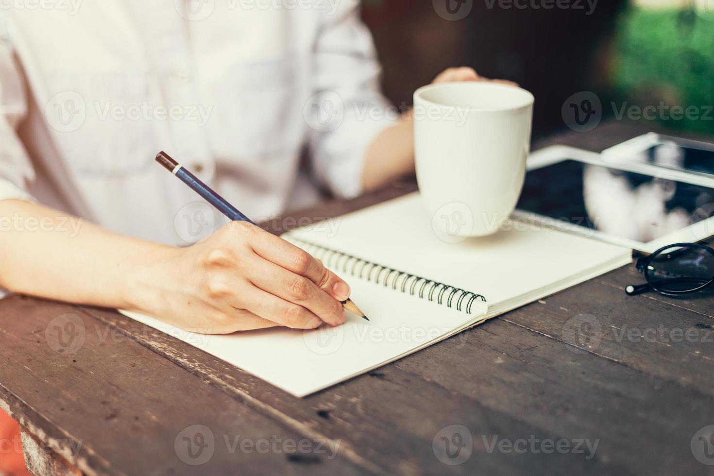 vrouw hand- met potlood schrijven Aan notebook. vrouw hand- met potlood schrijven Aan notitieboekje Bij koffie winkel. foto