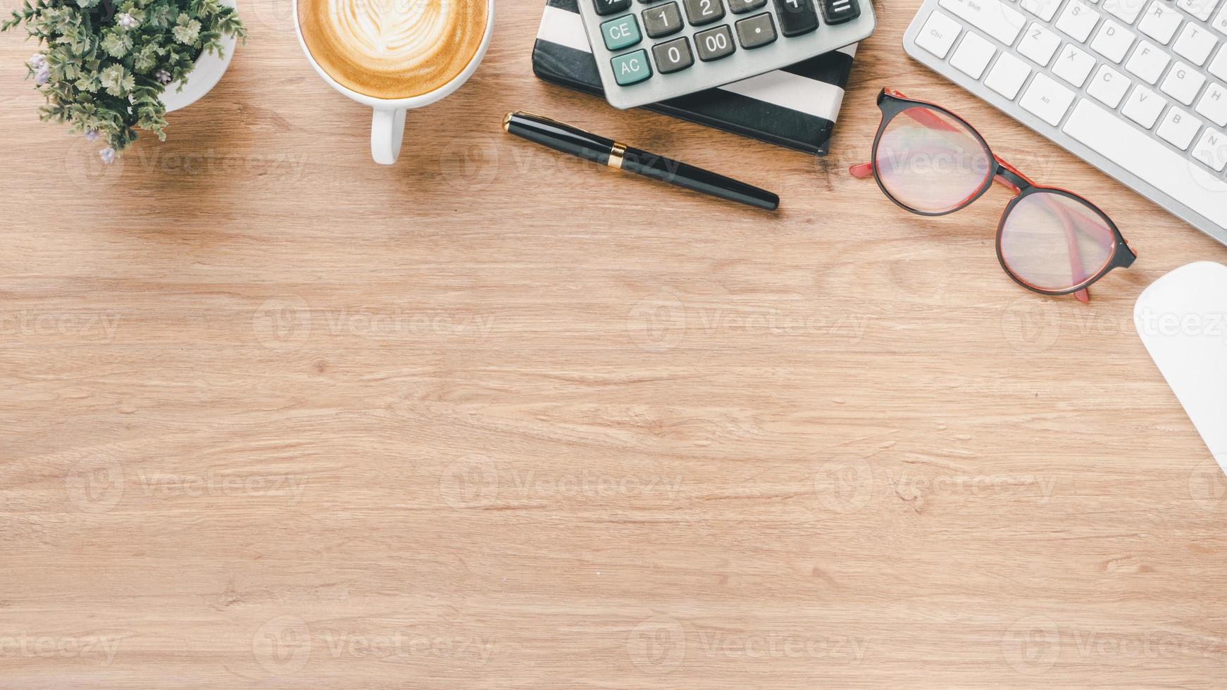 houten bureau werkplaats met toetsenbord computer, muis, lenzenvloeistof, pen, notitieboekje, rekenmachine en kop van koffie, top visie vlak leggen met kopiëren ruimte. foto