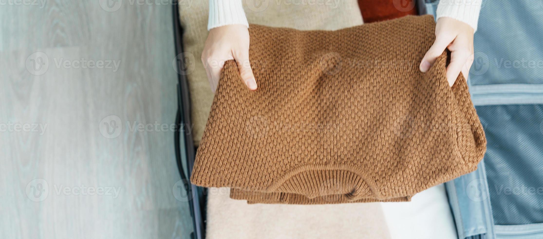 vrouw hand- inpakken haar winter kleren in bagage. tijd naar reis, reis, kom tot rust, voorjaar of herfst of winter seizoen en vakantie concepten foto