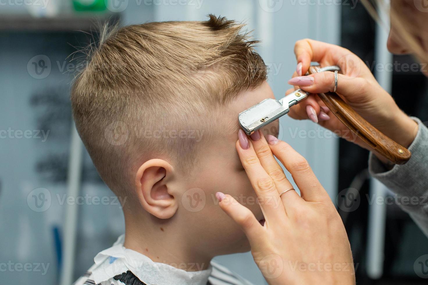 een jongen is zittend in een kapperszaak, aan het doen zijn haar- met een scheermes voor een kapsel foto