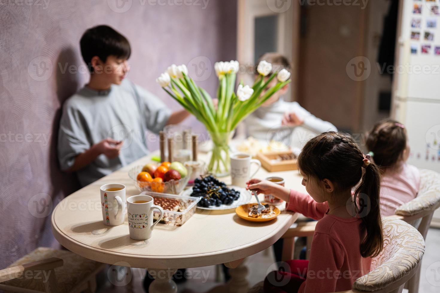 kinderen eten fruit en toetjes, drinken thee Bij huis in de avond keuken. foto