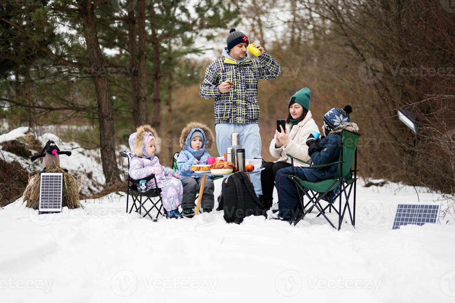 familie met drie kinderen in winter Woud uitgeven tijd samen Aan een picknick. foto