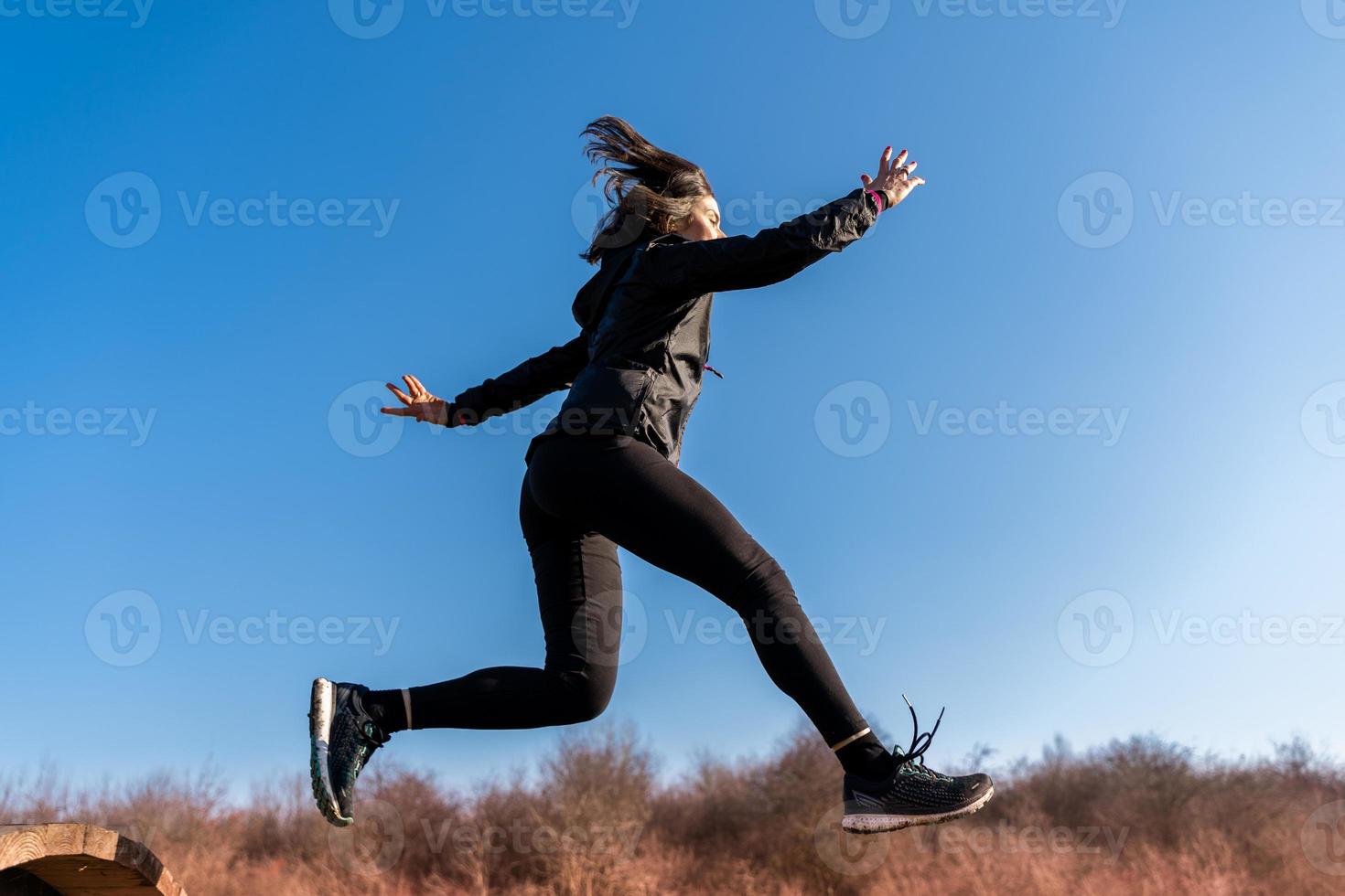 jong vrouw loper is jumping over- houten hindernissen in platteland foto