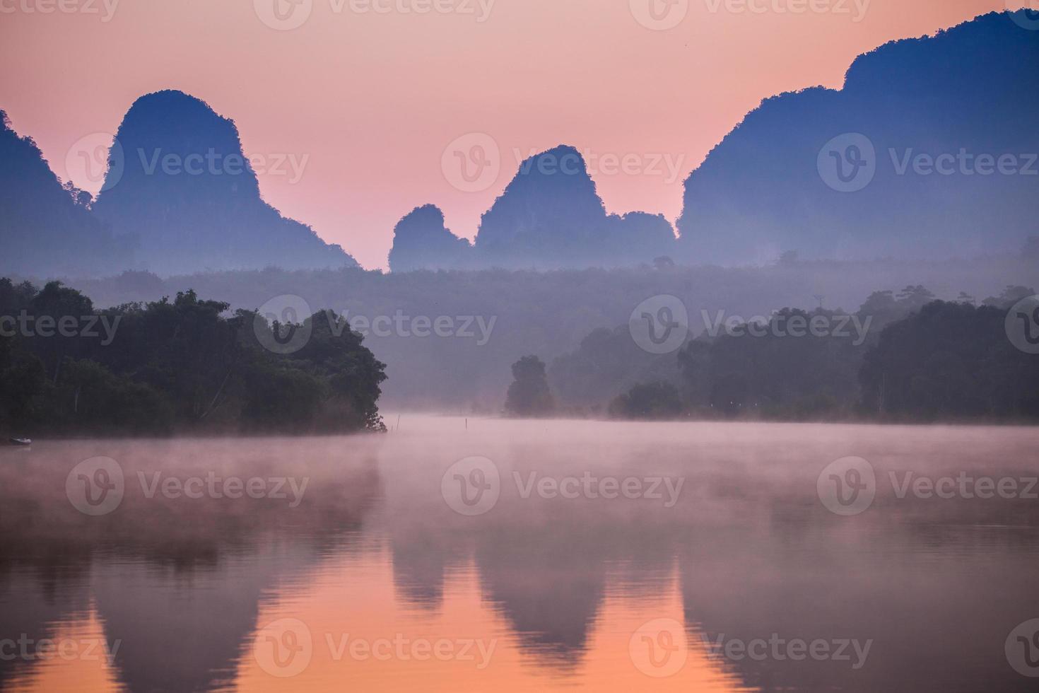 mistige zonsopgang boven water en bergen foto