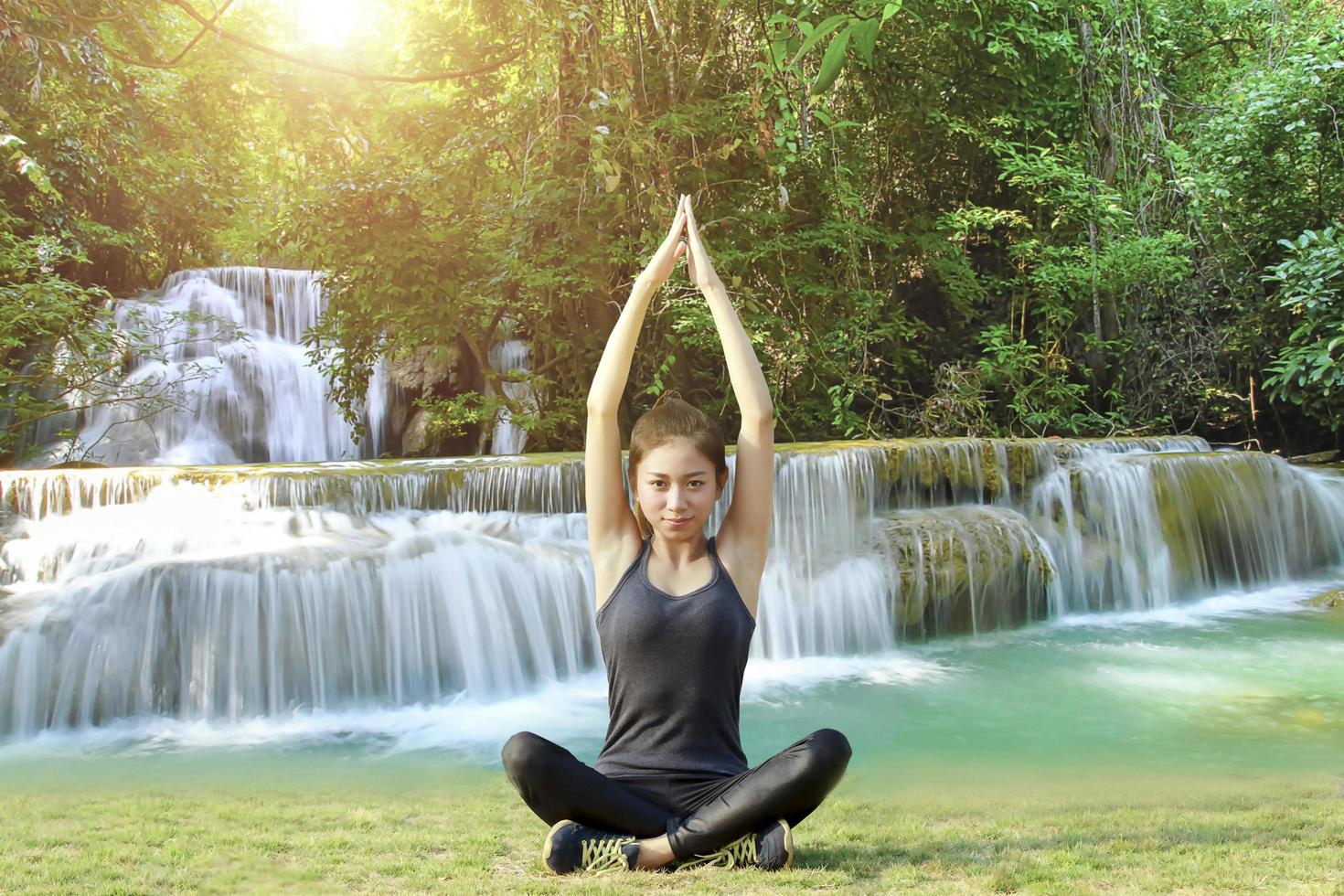 atletische Aziatische vrouw in yoga pose met waterval achtergrond foto