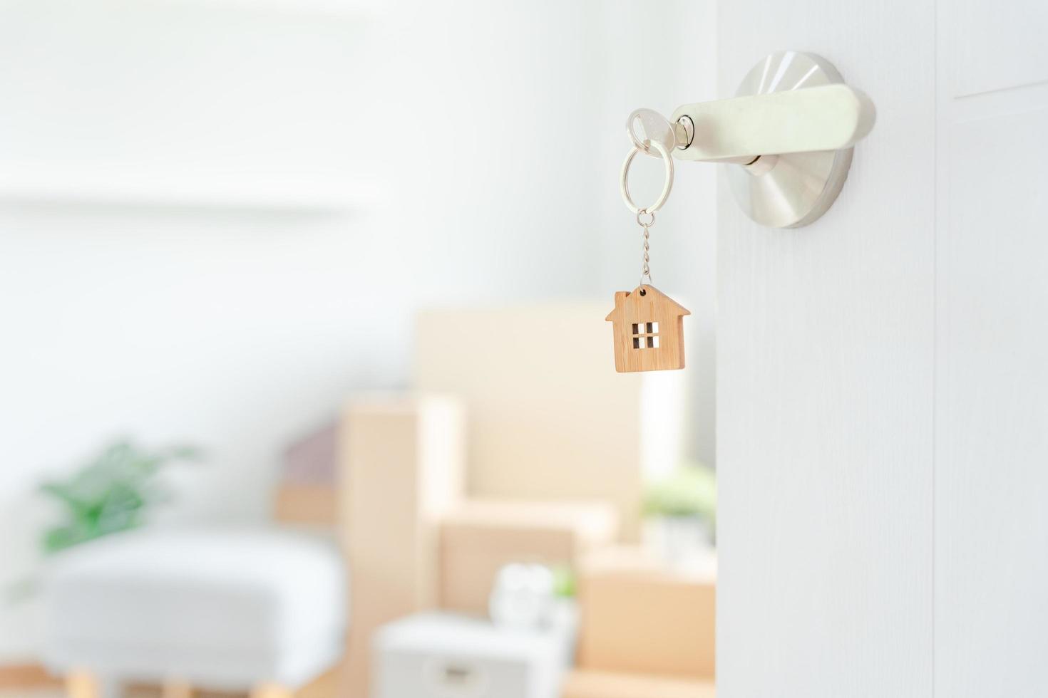 in beweging huis, verhuizing. de sleutel was ingevoegd in de deur van de nieuw huis, binnen de kamer was een karton doos met persoonlijk bezittingen en meubilair. Actie in de appartement of condominium foto