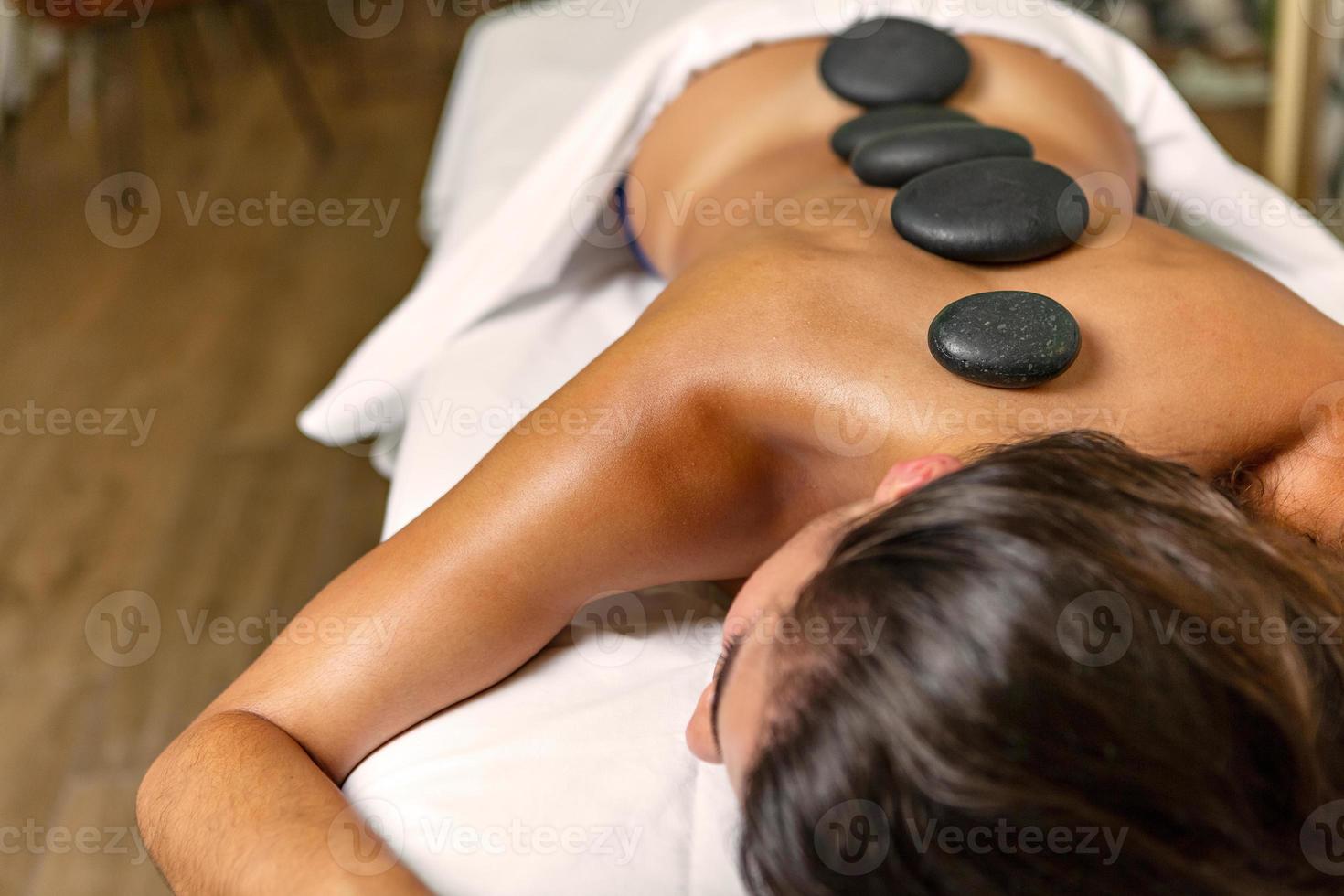 ontspannende vrouw met steen behandeling met heet vulkanisch stenen Aan terug in Gezondheid spa foto