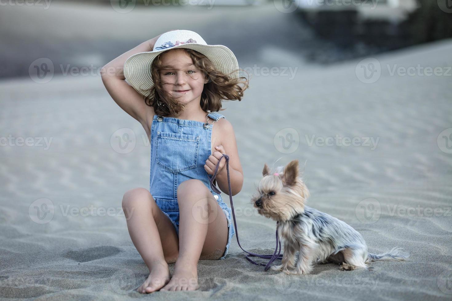 mooi meisje zittend Aan de strand zand Holding de riem van haar huisdier yorkshire terriër. foto