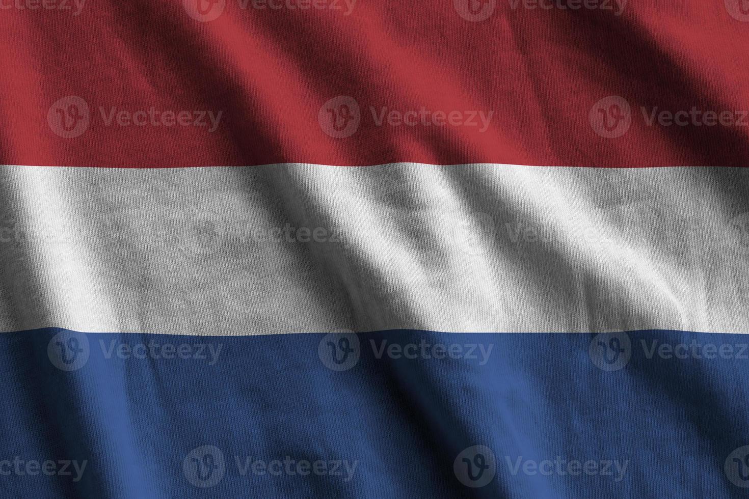 Nederland vlag met groot vouwen golvend dichtbij omhoog onder de studio licht binnenshuis. de officieel symbolen en kleuren in banier foto