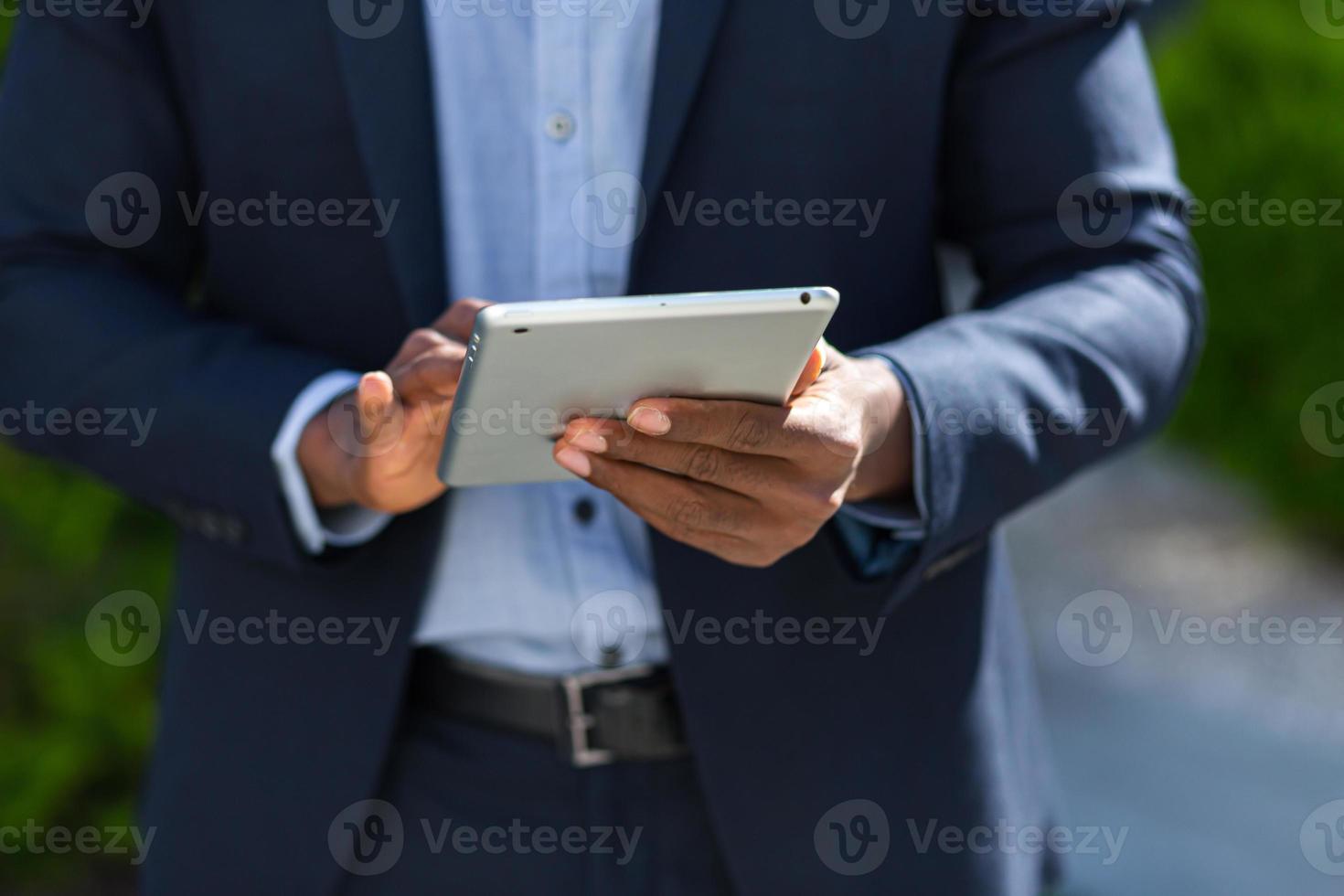 dichtbij omhoog van afro Amerikaans zakenman handen gebruik makend van tablet. een zwart bedrijf Mens in een formeel pak foto