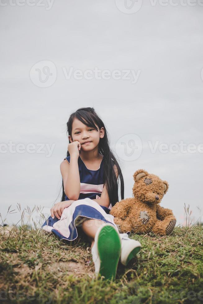 schattig Aziatisch meisje met teddybeer zittend in een veld foto