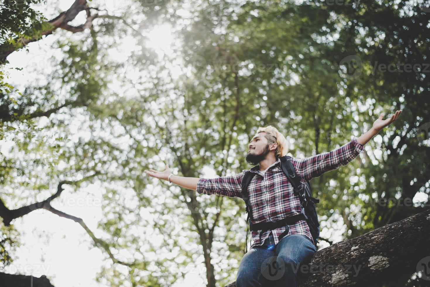 jonge wandelaar hipster man zittend op een boomtak met uitgestrekte armen foto