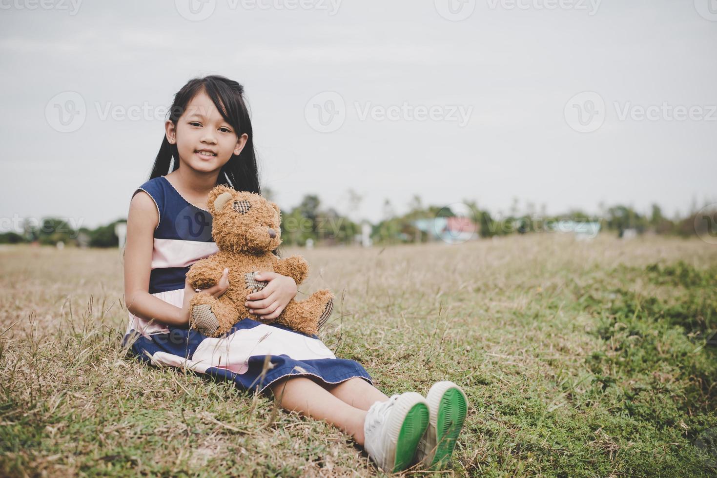 schattig Aziatisch meisje met teddybeer zittend in een veld foto