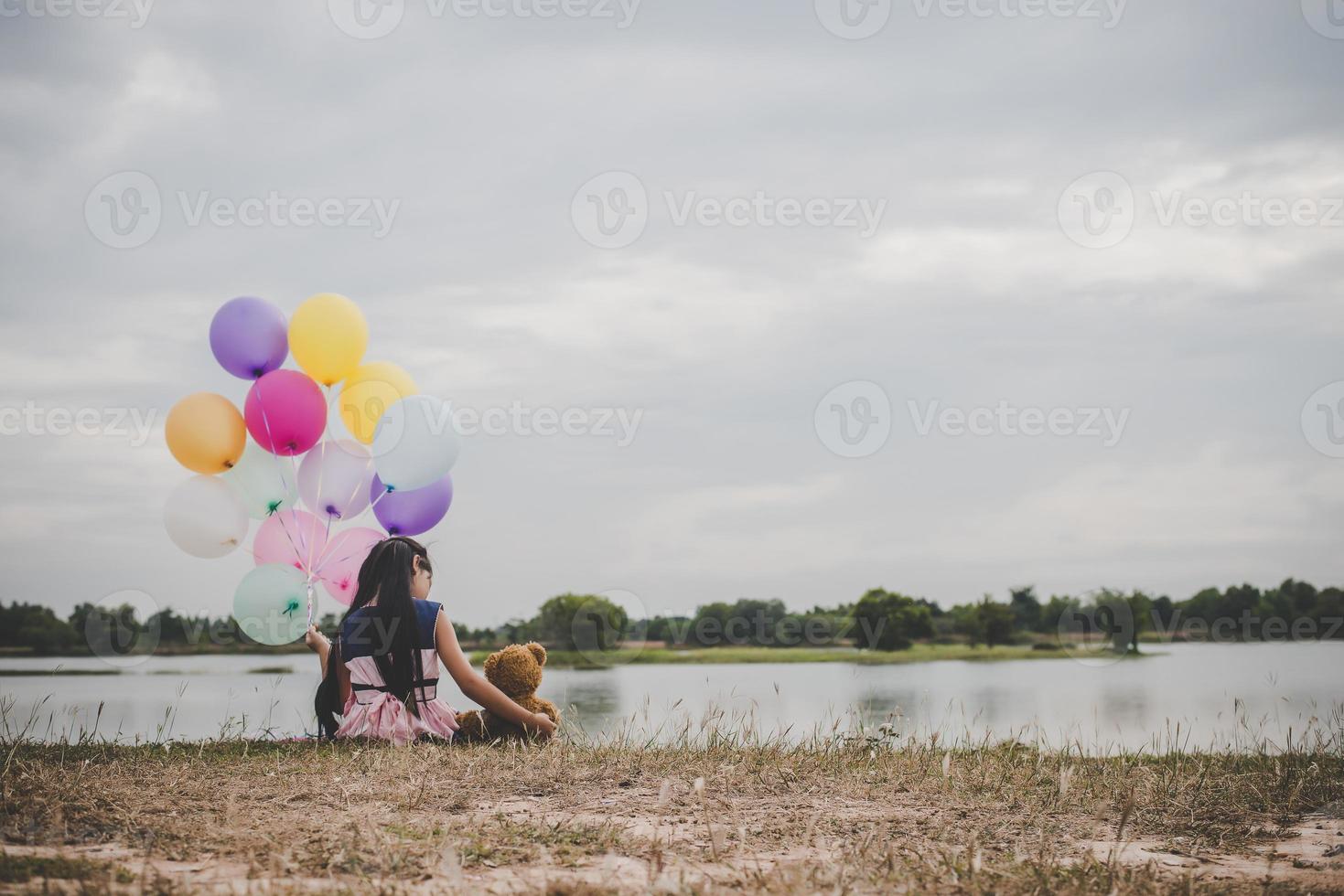 meisje met een teddybeer en ballonnen op weide veld foto