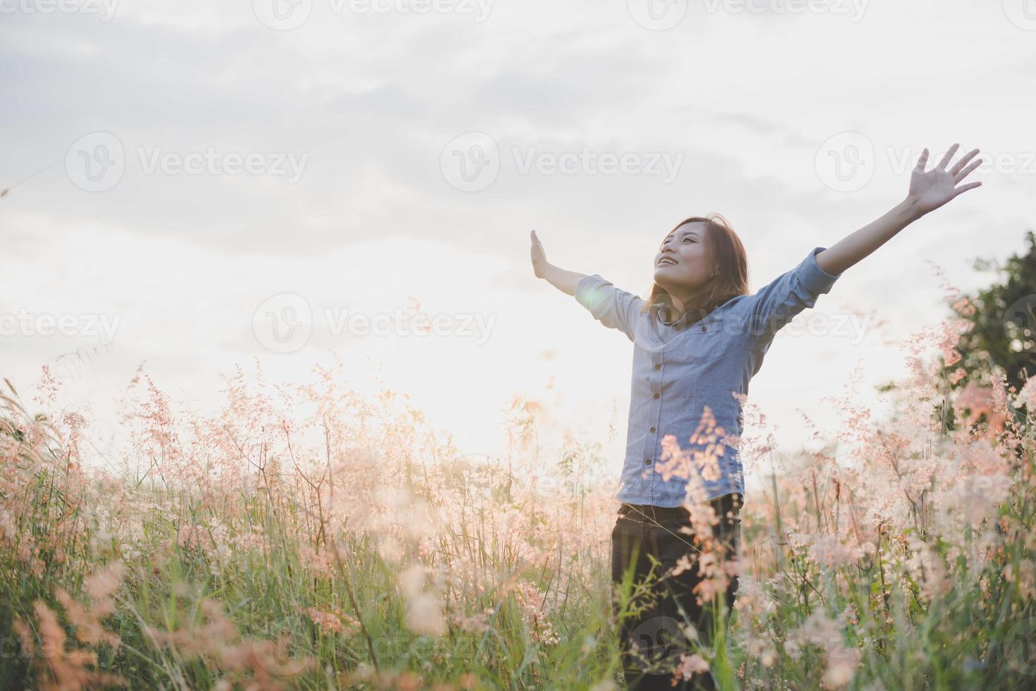 jonge mooie vrouw strekt haar armen in de lucht in een veld foto