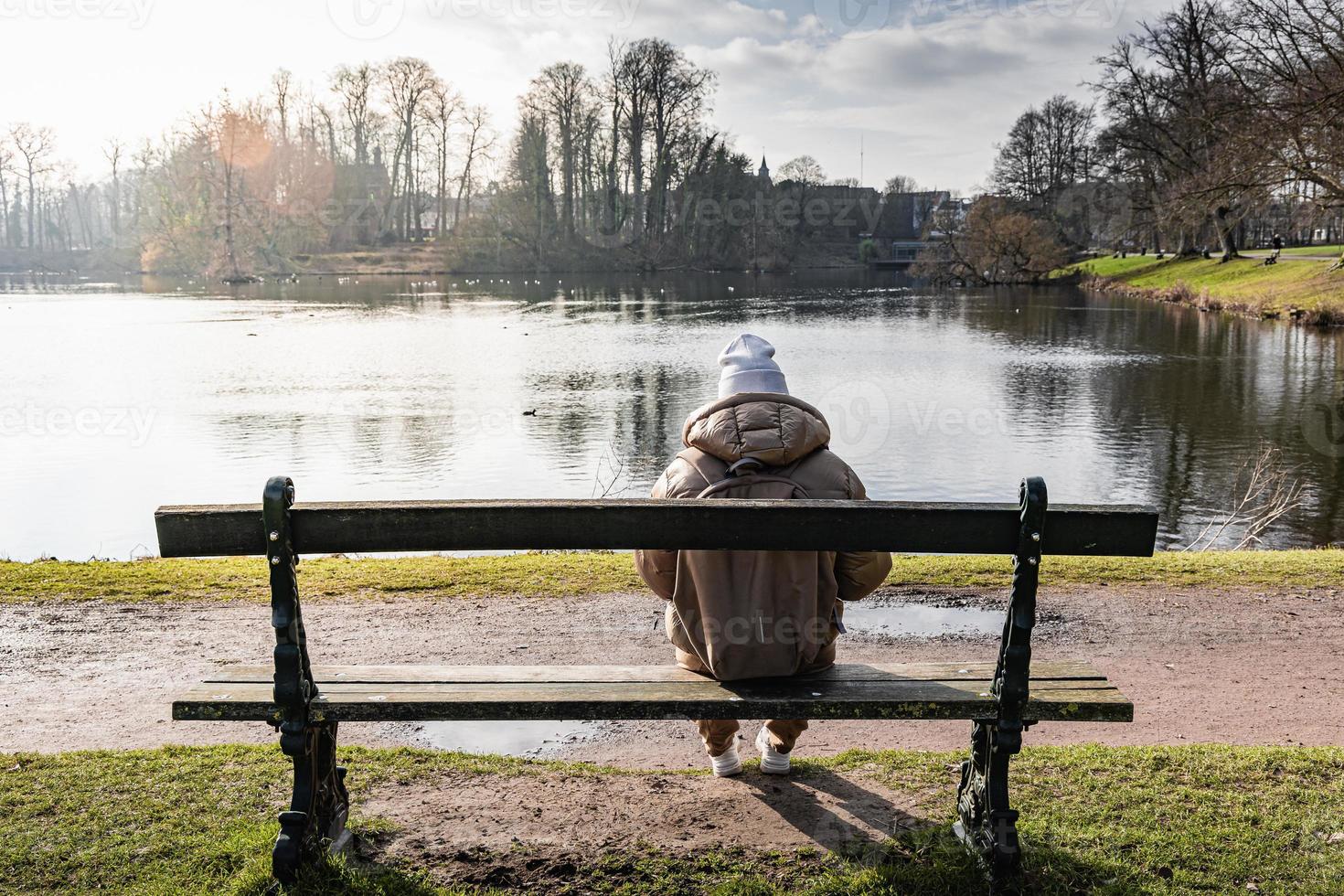 overpeinzing door de meer. een jong vrouw zittend Aan een park bank foto