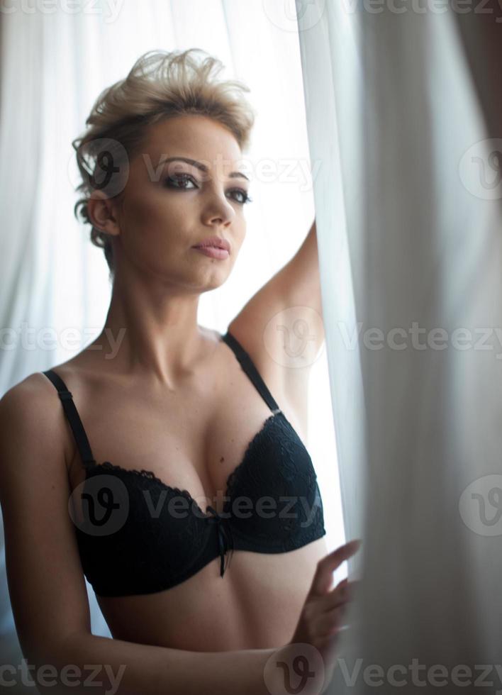 aantrekkelijk eerlijk haar- model- met panty en zwart beha en lang handschoenen poseren provocerend. mode portret van sensueel blond, studio schot. sensueel vrouw in zwart lingerie poseren tegen venster foto