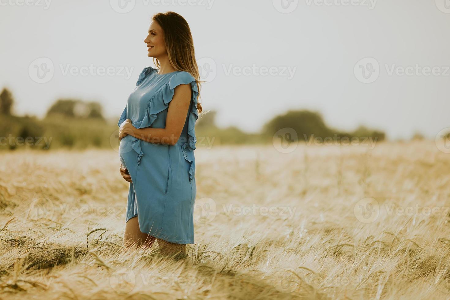 jonge zwangere vrouw in blauwe jurk buiten ontspannen in de natuur foto