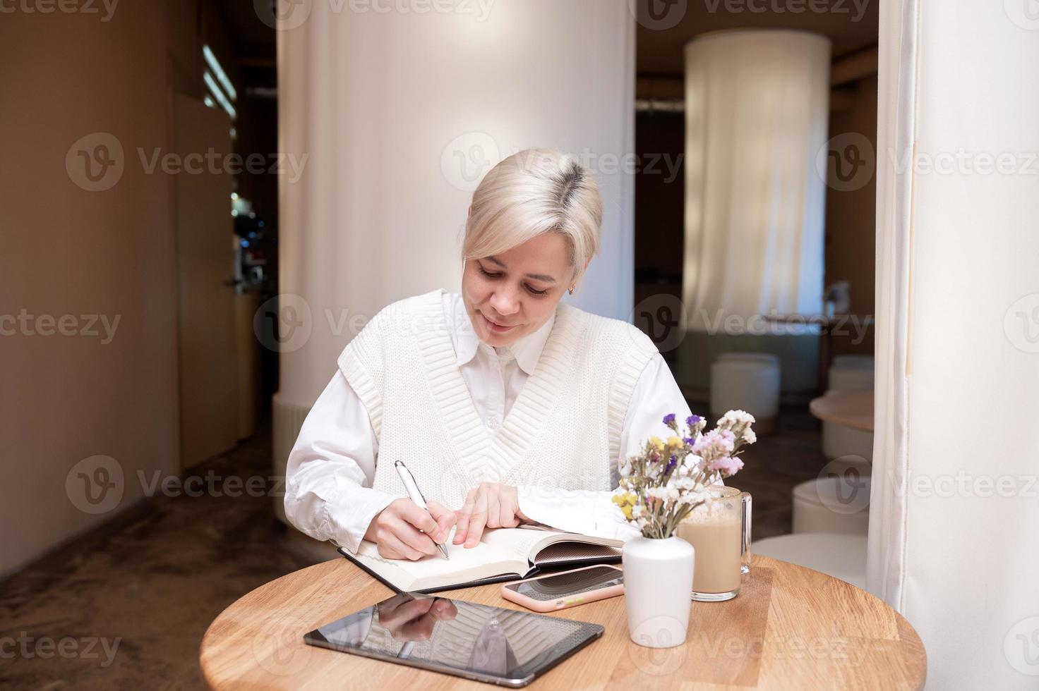 een schattig meisje is zittend in een cafe en maken aantekeningen in een dagboek foto