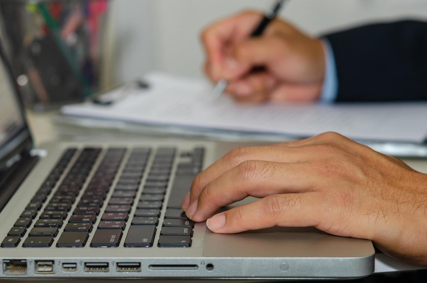 de hand van een zakenman op een computer en houdt een pen vast om zakelijke documenten op het bureau te schrijven foto