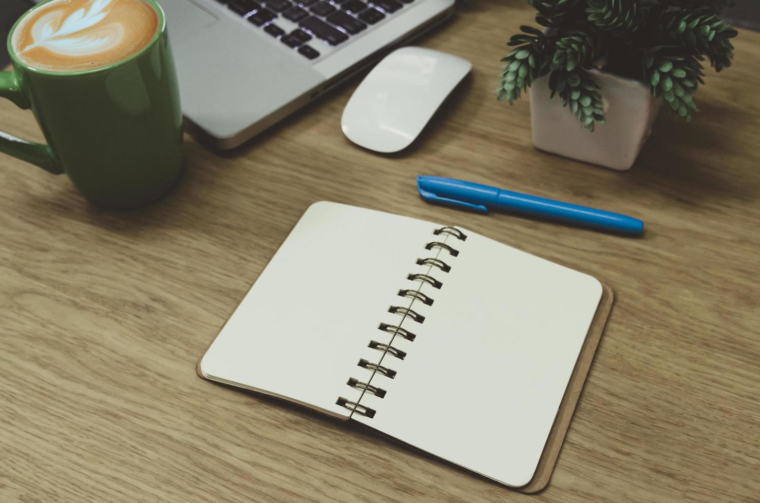 een blanco notebook liggend op een houten tafel en een groene koffiemok op de computer foto