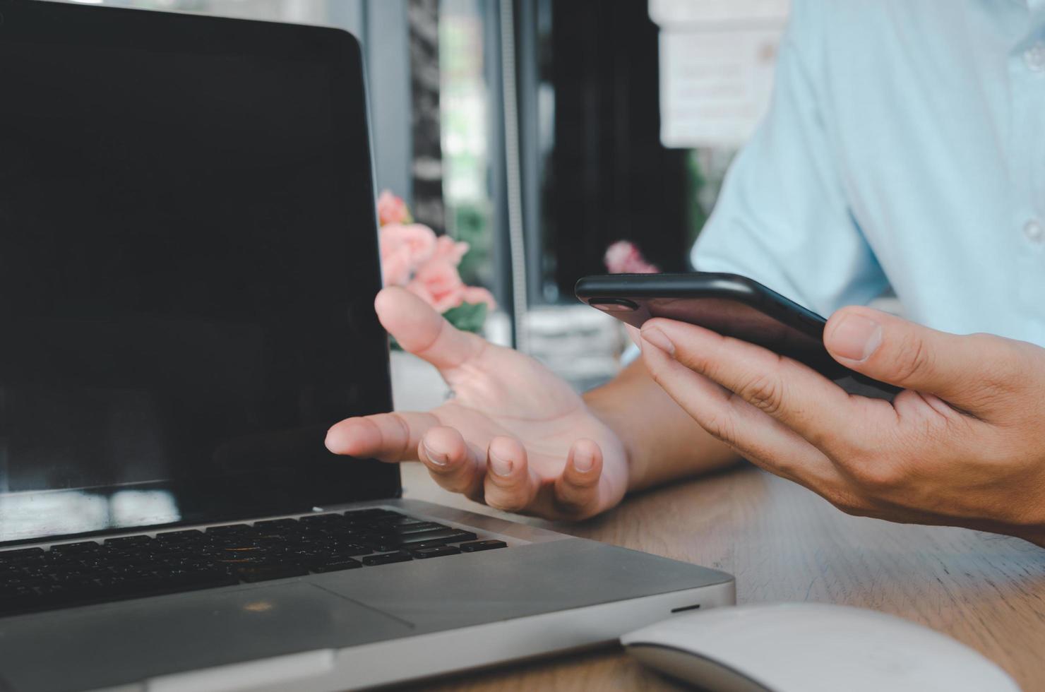 een zakenman die een mobiele smartphone en een computerlaptop gebruikt op een tafel die op internet zoekt foto