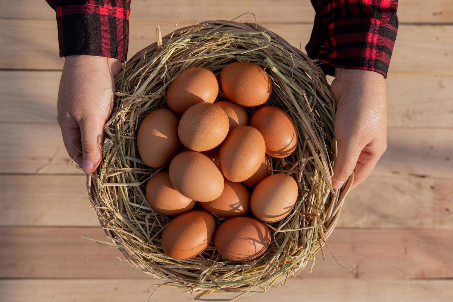 Dames slijtage rood gestreept overhemden, zetten vers eieren in een rotan manden geplaatst Aan houten vloer. foto