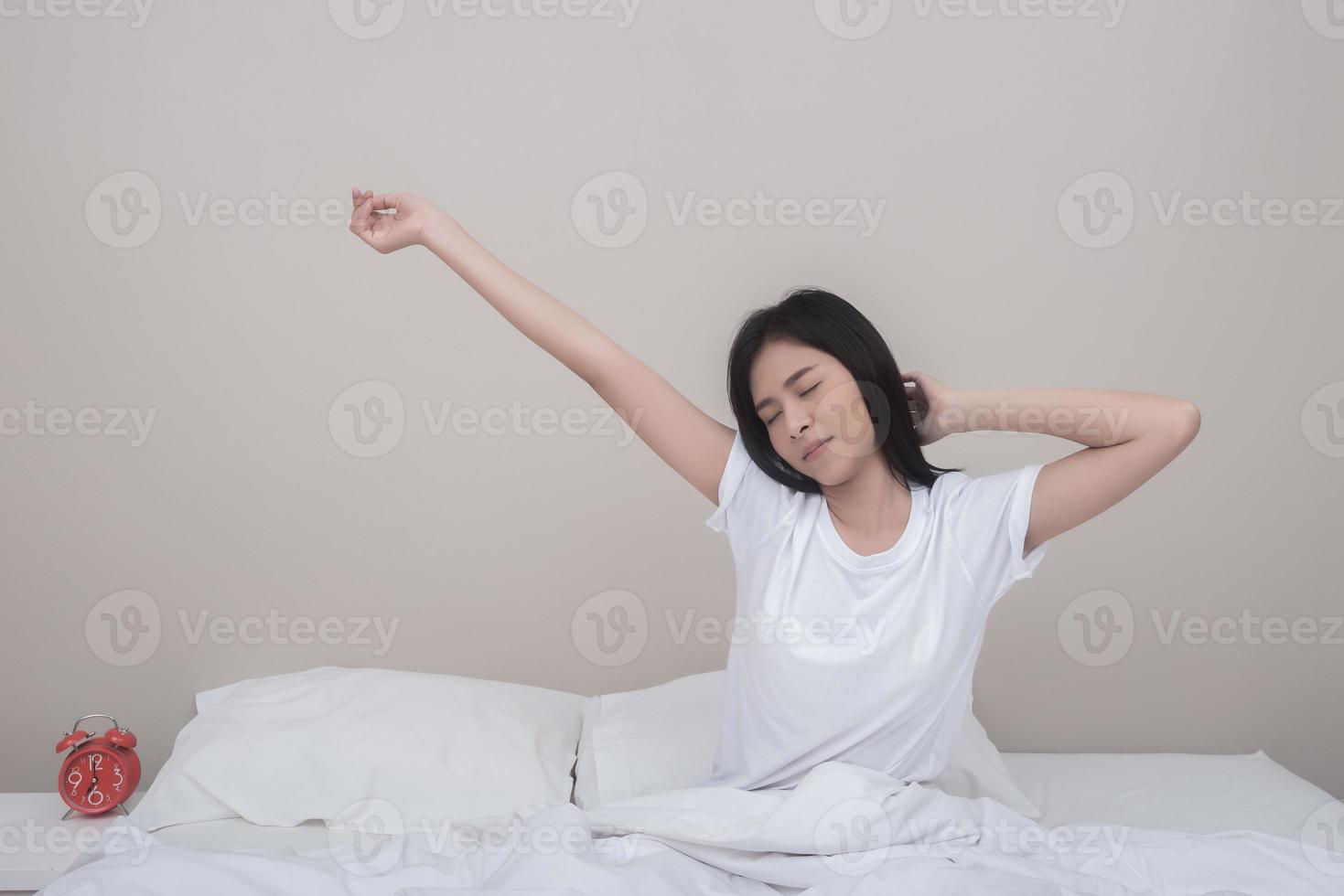 gelukkige vrouw die zich uitstrekt in bed thuis in de ochtend foto