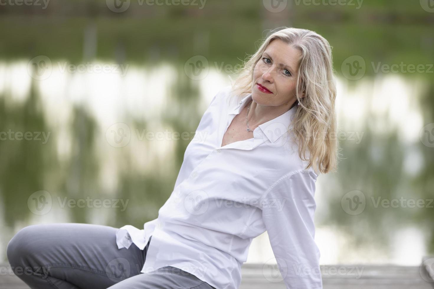 een mooi middelbare leeftijd Europese vrouw. vijftig jaar oud blond vrouw in een wit overhemd Aan de achtergrond van natuur. foto