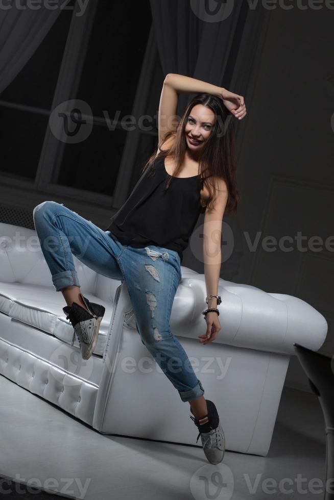 charmant brunette poseren zittend Aan een sofa foto