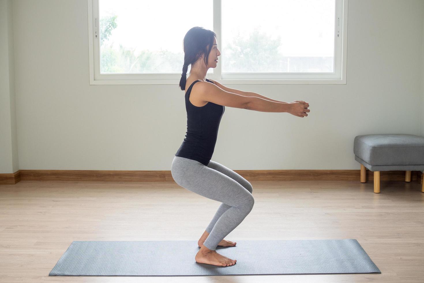 kant visie van een vrouw staand met armen uitgebreid naar beide zijden en knieën een beetje lager. bereiden voor yoga in de kamer. foto