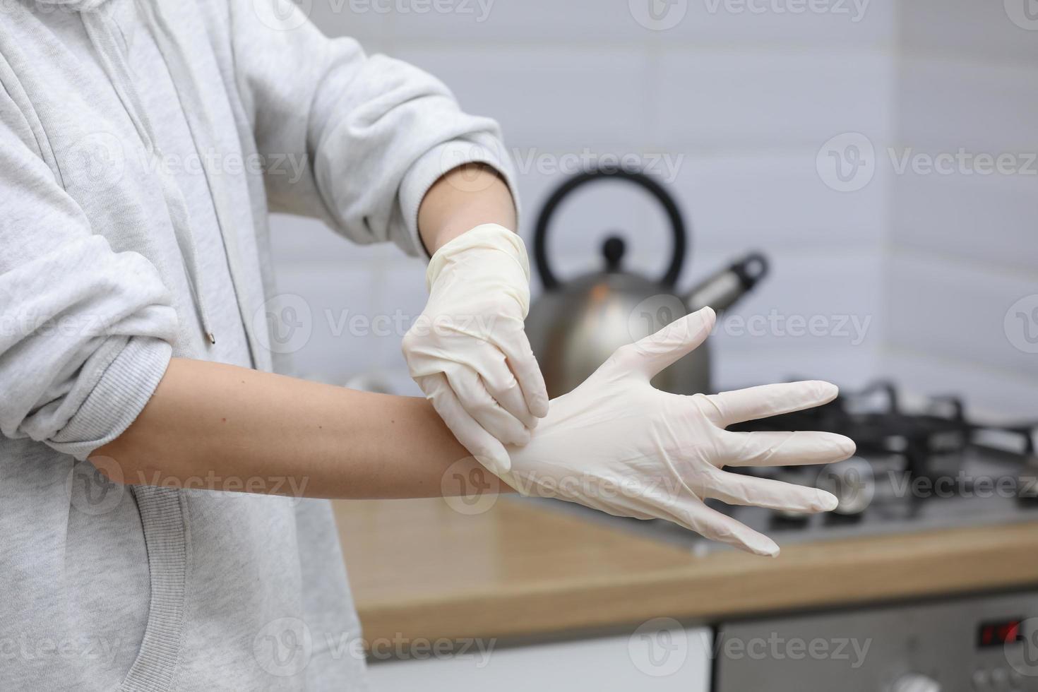 jong vrouw zetten Aan beschermend handschoenen Aan handen terwijl werken van huis of Bij de kantoor werk door de tafel laptop in dag voorkomen virus verspreiding gedurende epidemie in quarantaine. selectief focus foto