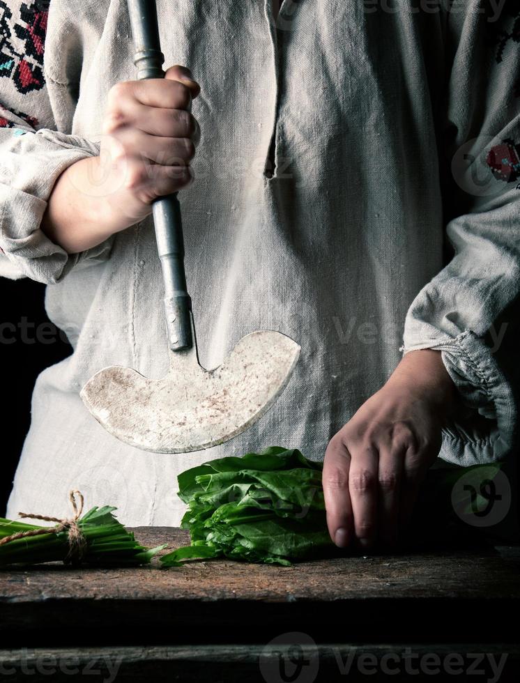 vrouw in een grijs linnen jurk is snijdend groen bladeren van vers zuring Aan een houten snijdend bord foto