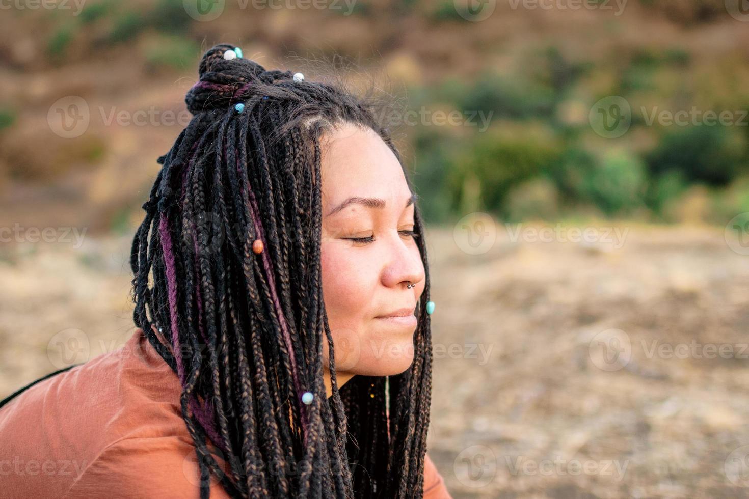 dichtbij omhoog portret van mooi Europese vrouw met lang Afrikaanse vlechtjes en Gesloten ogen Aan een achtergrond van natuur. foto