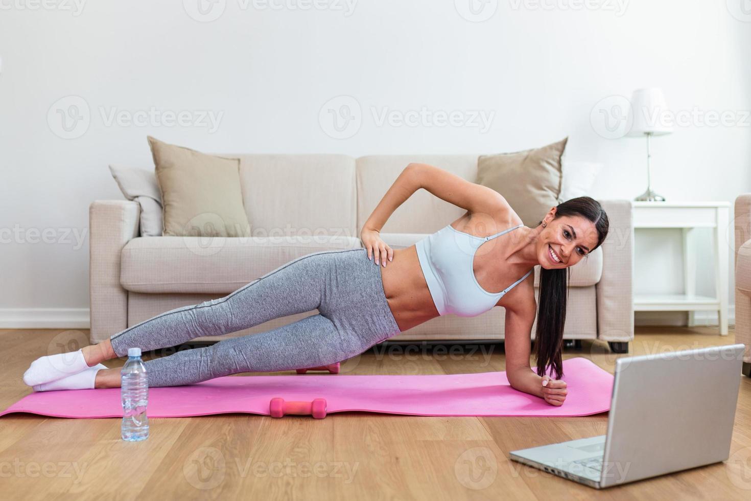 meisje opleiding Bij huis, aan het doen training en aan het kijken videos Aan laptop, opleiding in leven kamer. mooi vrouw is aan het doen kant plank oefening. ze is aan het kijken video Aan de internet en herhalen de taken foto