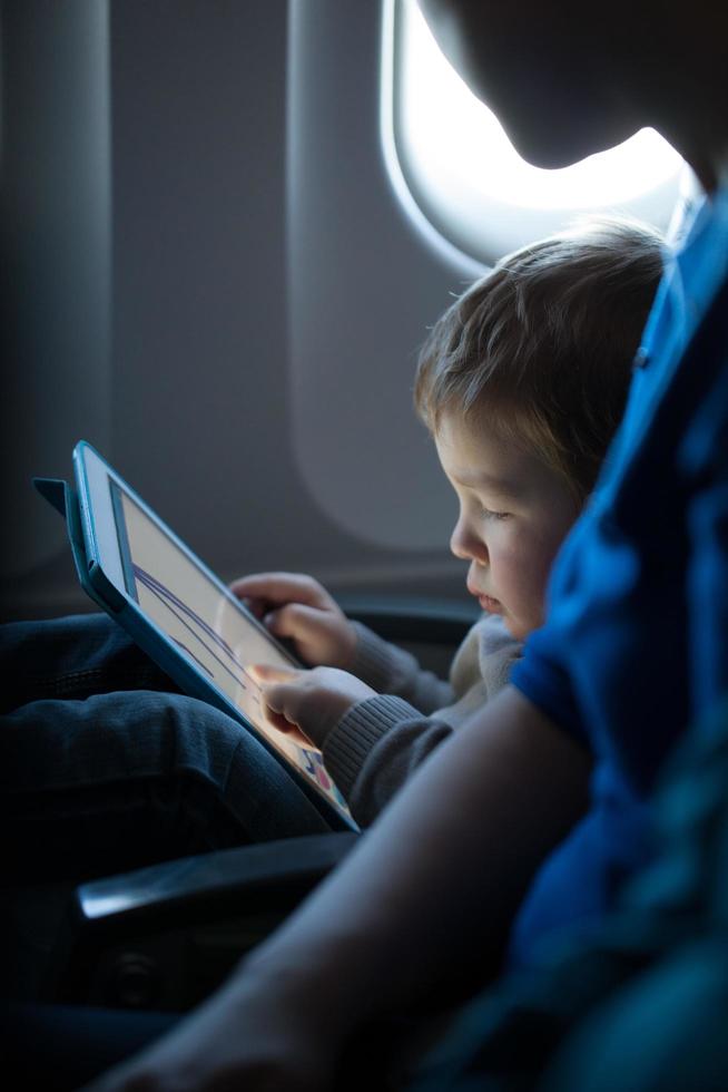 kleine jongen speelt met een tablet in een vliegtuig foto