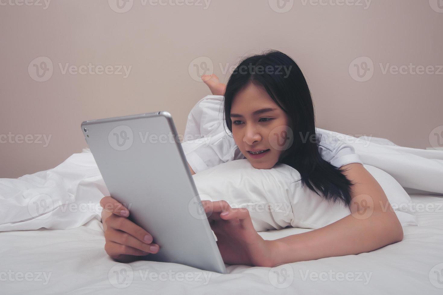 vrouw met behulp van tablet lachend liggend op bed thuis in de ochtend foto