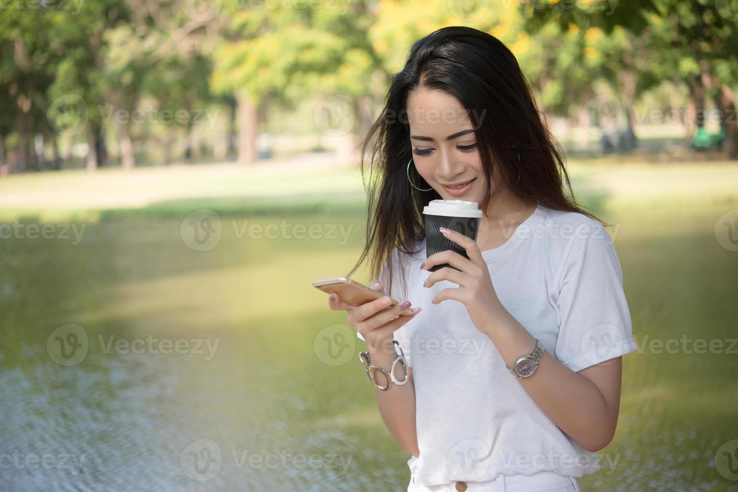 jonge vrouw met koffiekopje tijdens het gebruik van smartphone buitenshuis foto