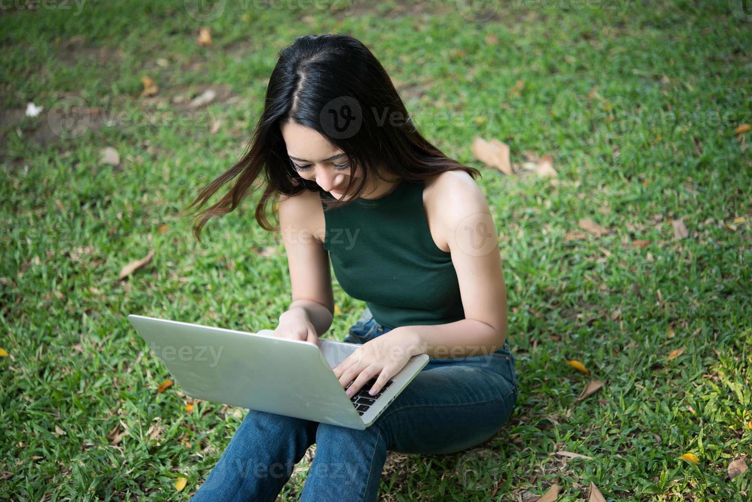 jonge mooie vrouw zittend op het groene gras en met behulp van laptop in het park foto