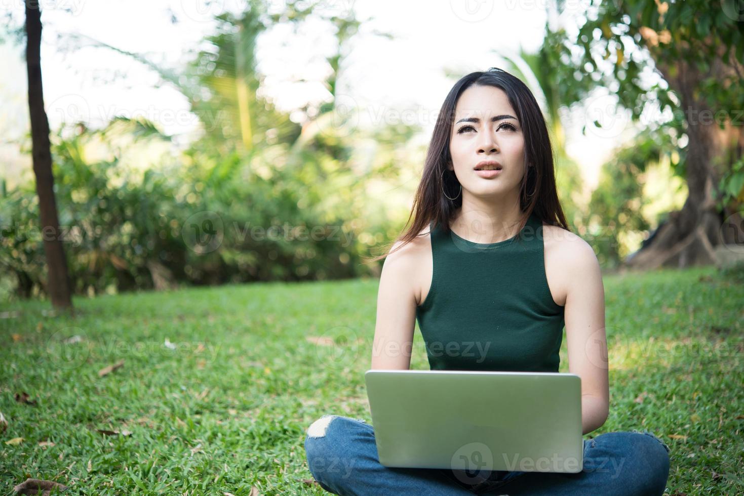 jonge mooie vrouw zittend op het groene gras en met behulp van laptop in het park foto