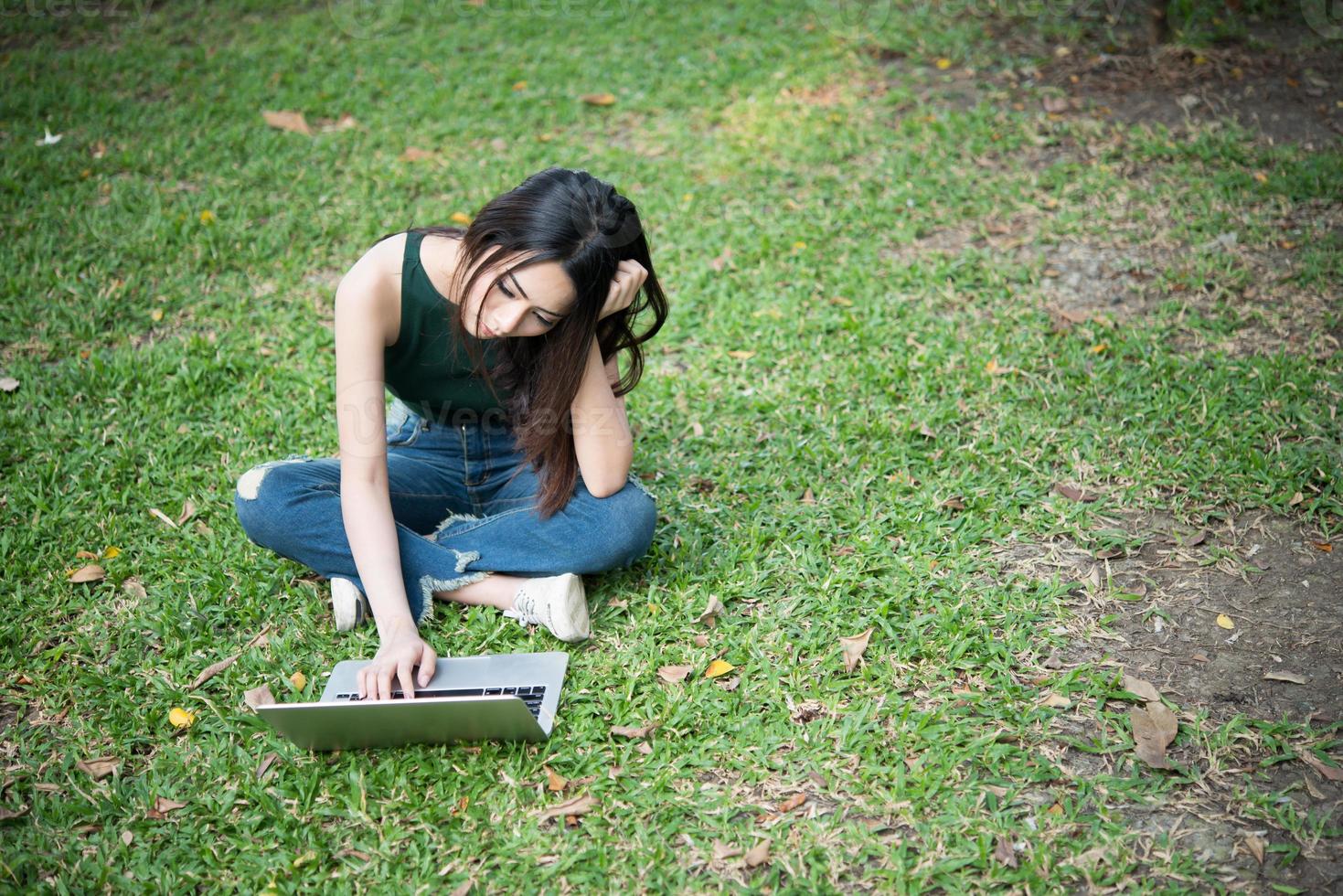 jonge mooie vrouw zittend op het groene gras en met behulp van laptop in het park foto