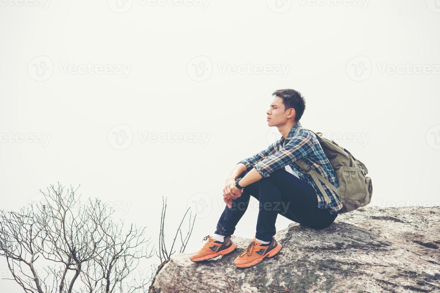 jonge hipster wandelaar met rugzak zittend op de top van de berg foto