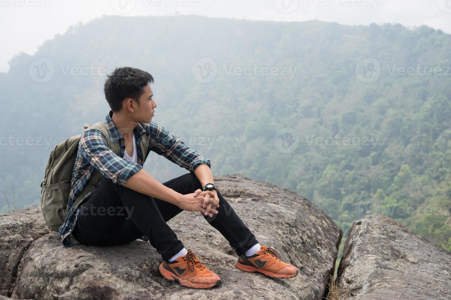 jonge hipster wandelaar met rugzak zittend op de top van de berg foto