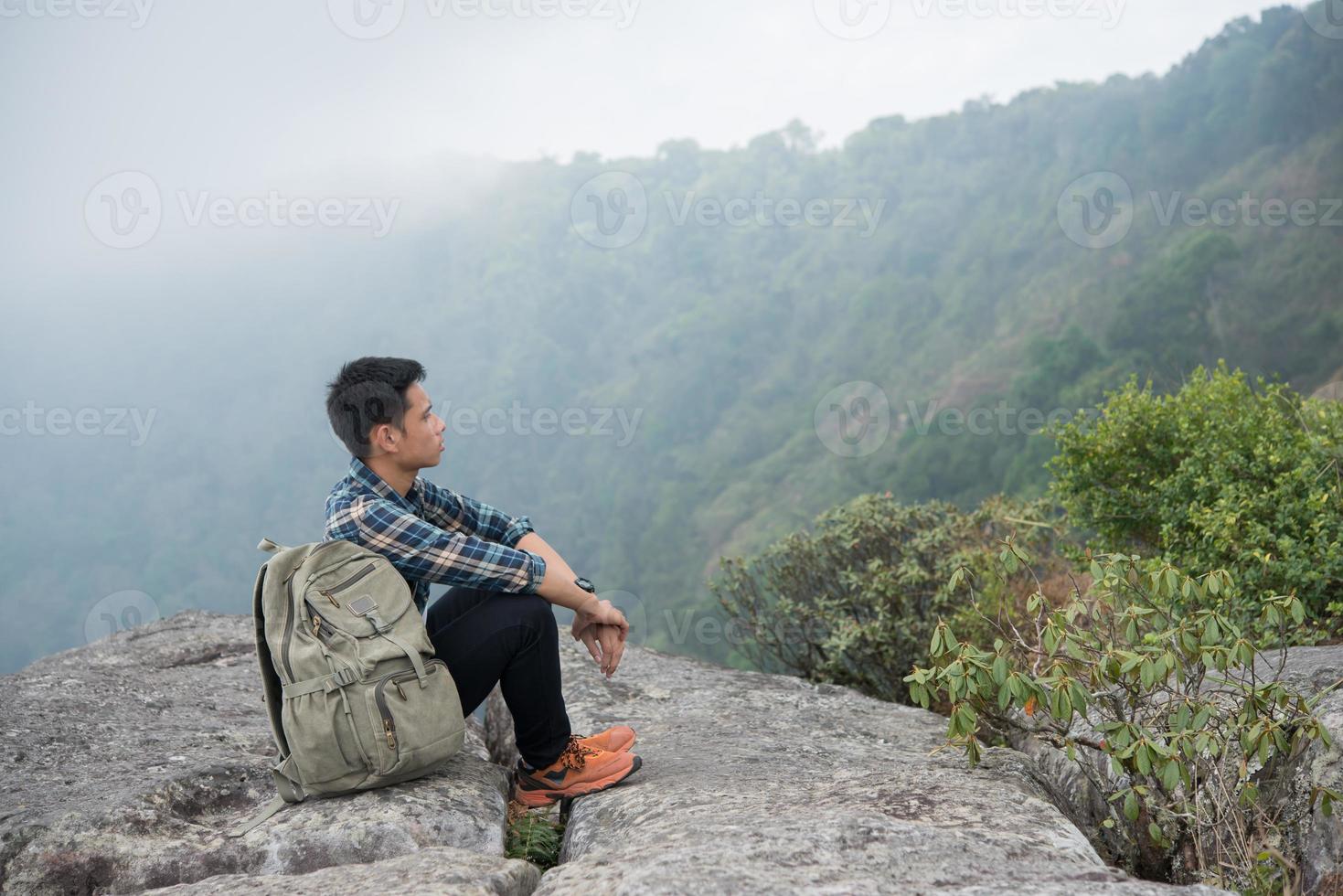 jonge hipster wandelaar met rugzak zittend op de top van de berg foto