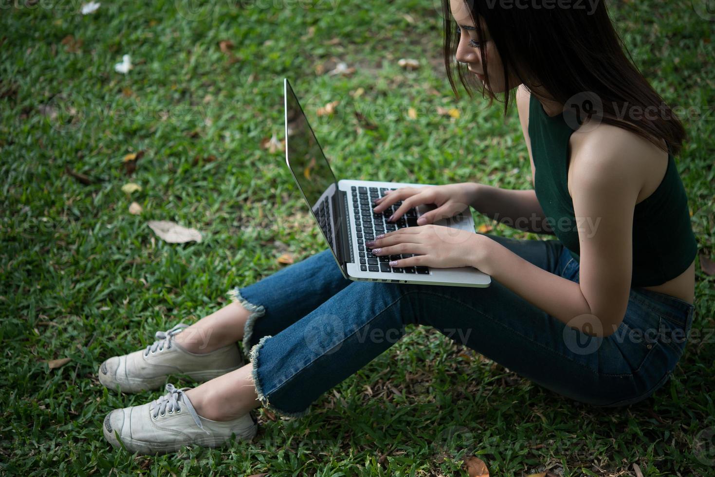 jonge mooie vrouw zittend op het groene gras en met behulp van laptop in het park foto