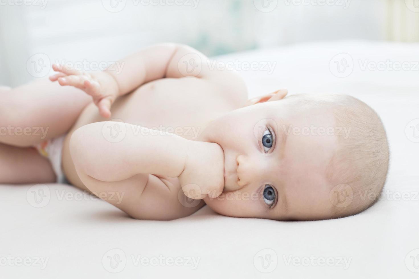 babymeisje liggend met hand in de mond foto