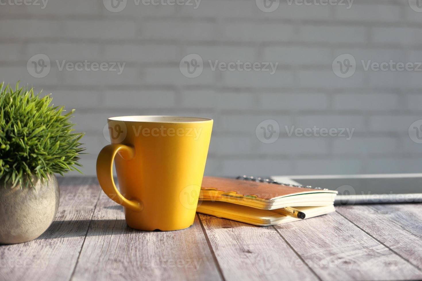 Kladblok, digitale tablet en gele koffiemok op tafel in de zon foto