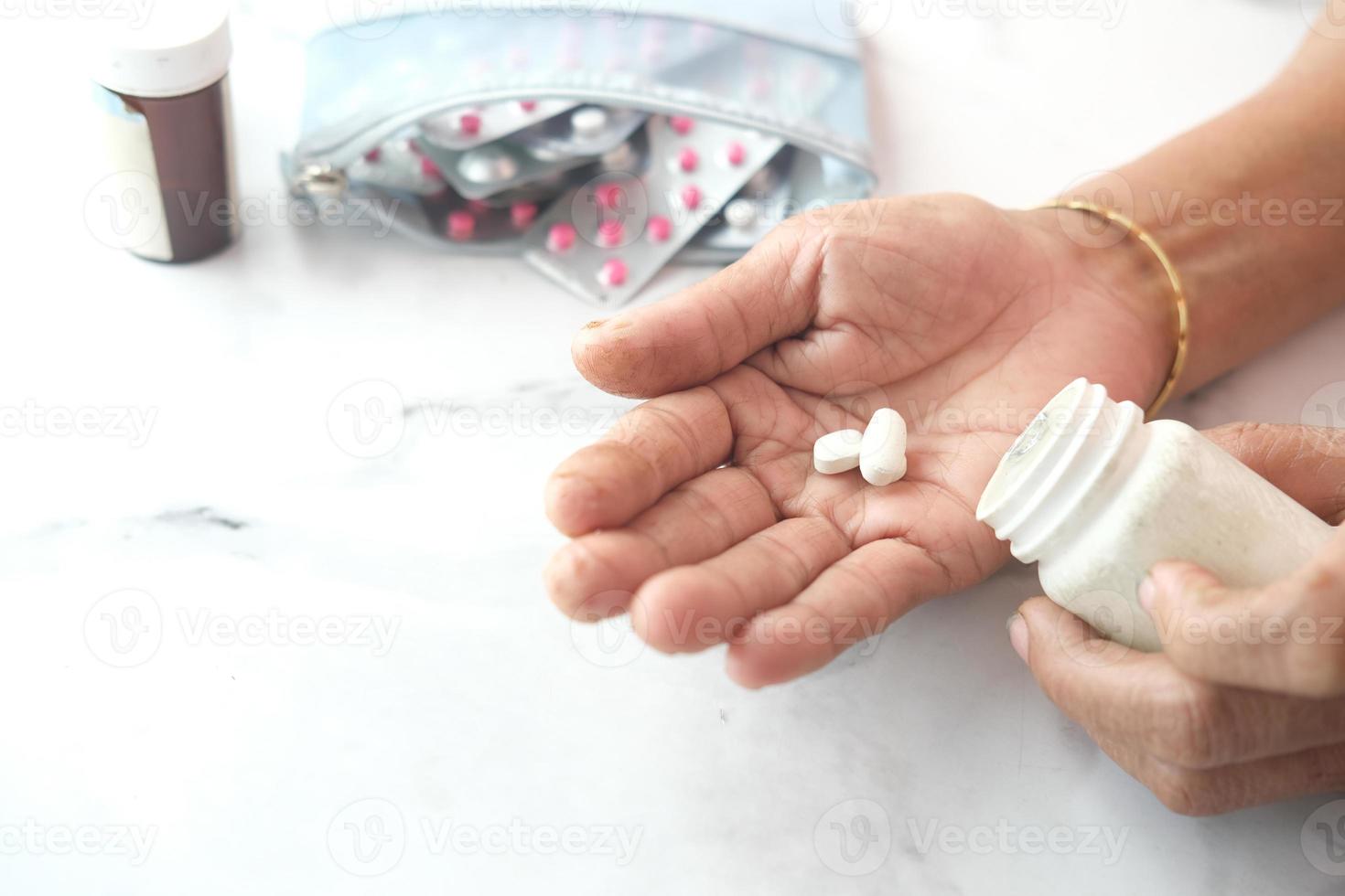 hand van een oudere vrouw met medicijn dat uit de container is gemorst foto