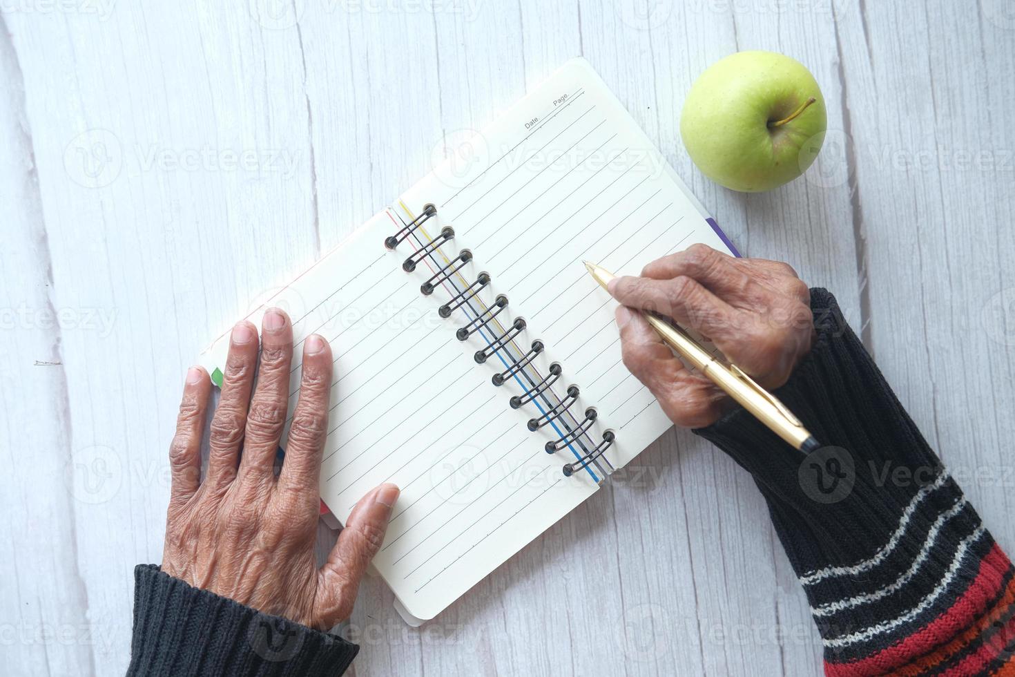 close-up van senior vrouw hand schrijven op Klad blok foto