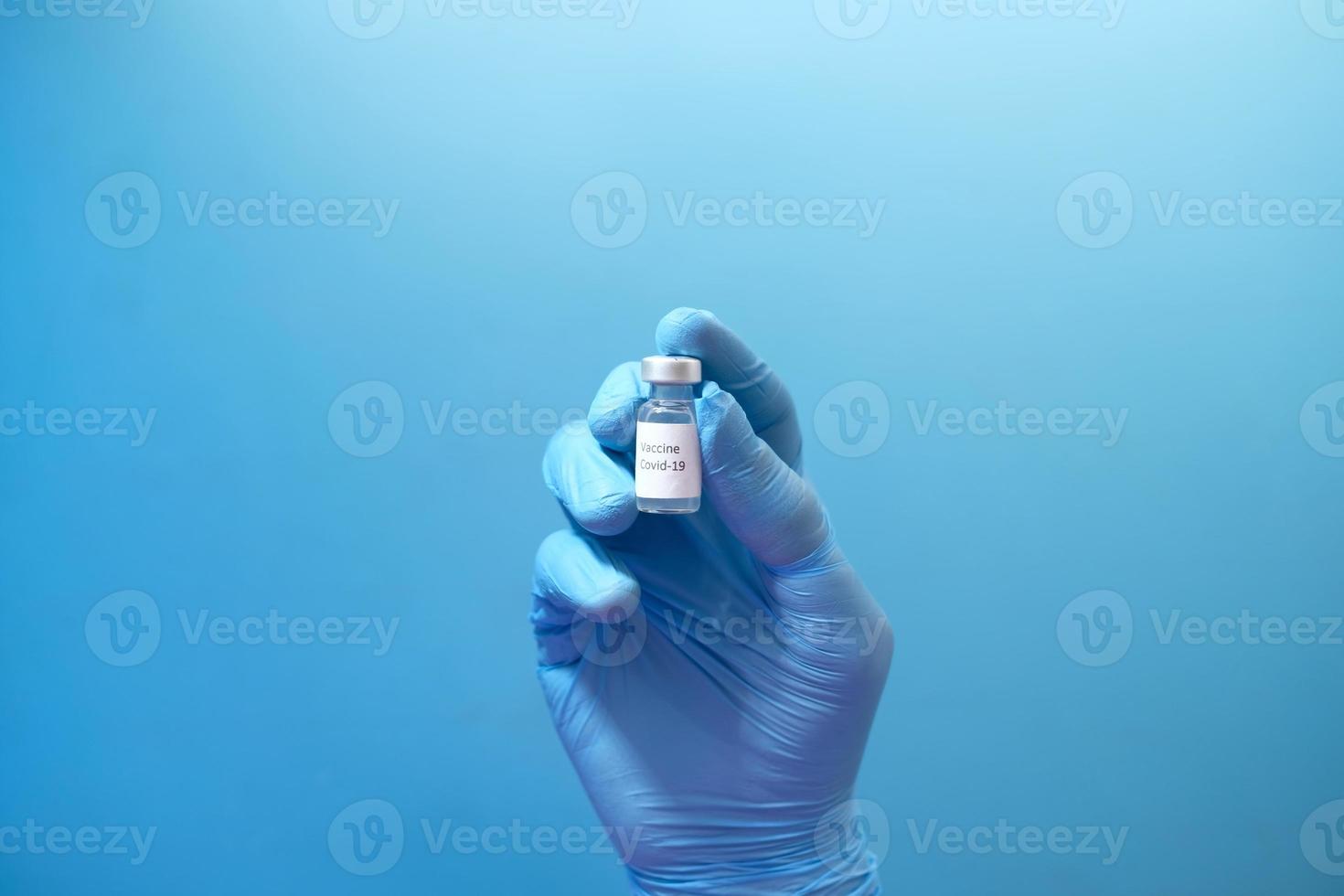 dien latexhandschoenen in die coronavirusvaccin op blauwe achtergrond houden foto